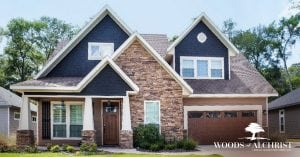 This two-story, dark gray home has wood finishing on the front door and garage, with brick accents. Luxury homes are built at Woods of Alchrist.